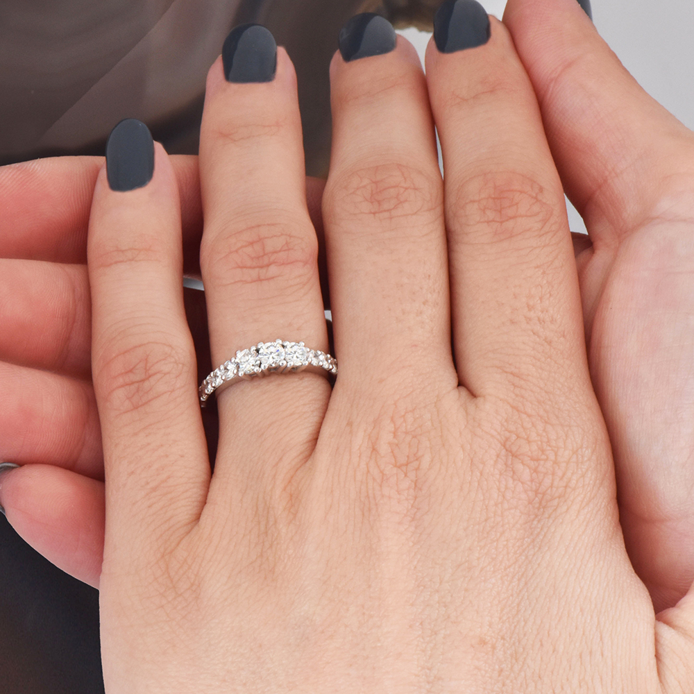 טבעת אירוסין זהב לבן עם שלוש יהלומים מרכזיים ויהלומים קטנים בחישוק על אצבע אישה